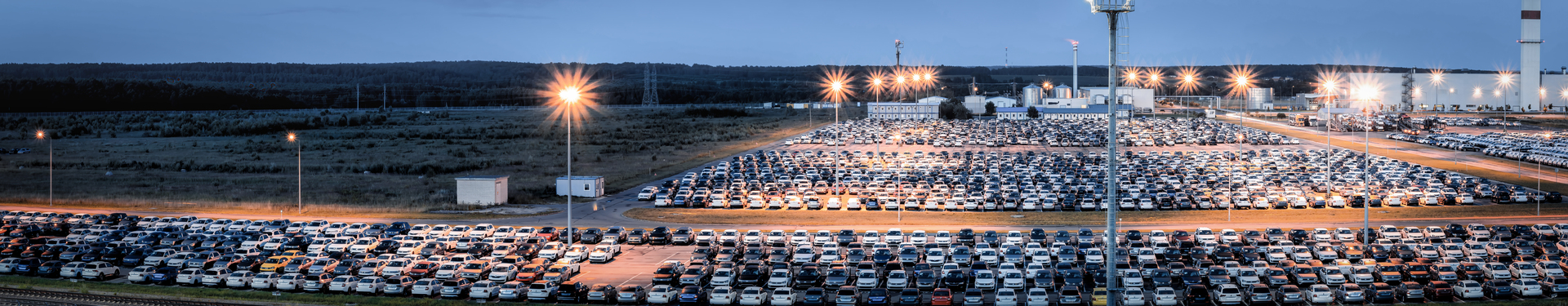 A vast parking lot filled with new cars at a distribution center of an automobile factory, illuminated by tall street lights at night.